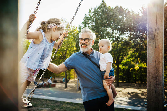 Grandfather with grey hair plays with his grandchildren on the swings