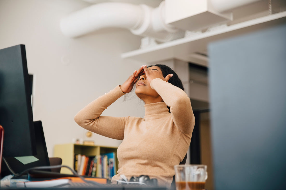 Tired woman sits at desk with head in hands