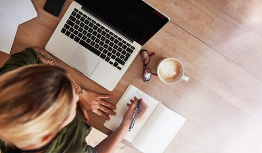 Woman writes to-do list next to laptop